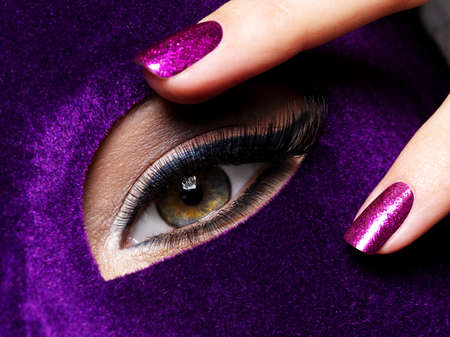 Woman's fingers with purple nails about eye. Macro photo
