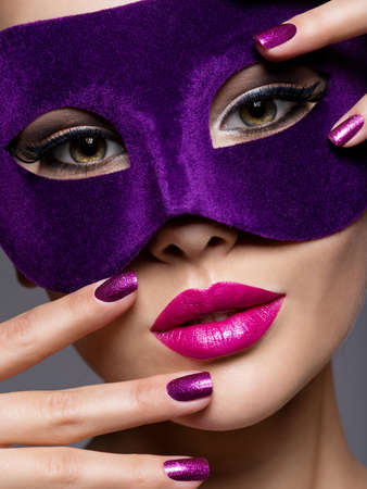 Portrait of a beautiful  woman with purple nails and violet theatre mask on face.の写真素材