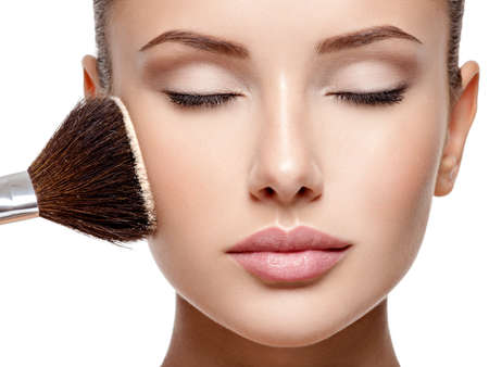 Closeup portrait of a woman  applying dry cosmetic tonal foundation  on the face using makeup brush.の写真素材
