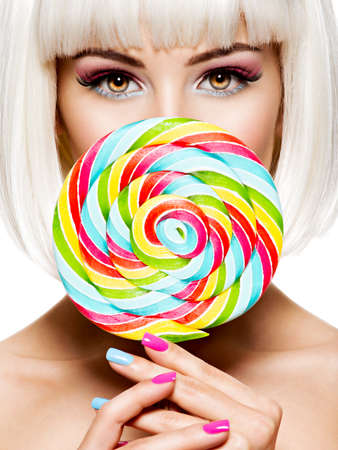 Face of a beautiful  girl with pink eye make-up and multicolor sweet candy. Fashion model posing on white backgroundの写真素材