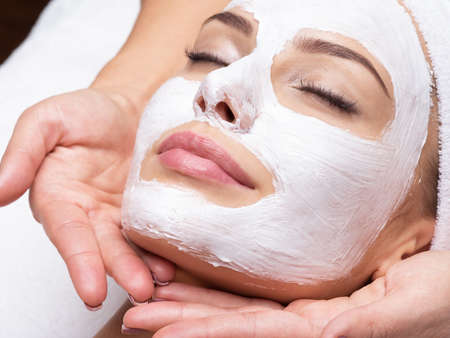Spa massage for young woman with facial mask on faceの写真素材