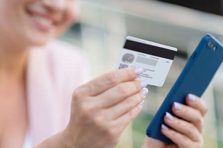 Businesswoman with a credit card and phone makes purchasing outdoors. Successful  woman is using...