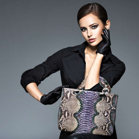 Beautiful woman in black  holds fashion handbag posing at studio