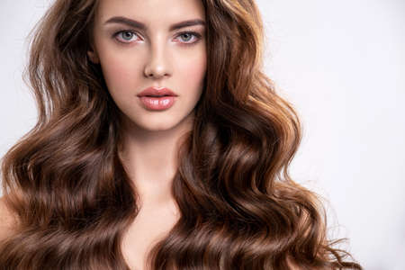 Portrait of a young beautiful woman with a long hair. Attractive fashion model with  brown hair - isolated on white background. Young girl with wavy hair looks to the camera.の写真素材