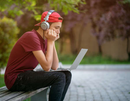 Teenage boy with a laptop in the park. Handsome young man works on a notebook, outdoors. Caucasian...