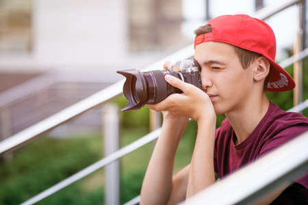 Teenage boy taking photos outdoors. Young man works reporter, outdoors. Caucasian guy holds a photo...
