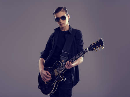 Fifteen years old guitarist with a  black electric guitar. Teenage musician holds guitar, posing at...