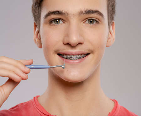 Teen boy cleaning braces.  Young man taking care of his teeth. Dental hygiene. Teenager brushes braces, isolated on white.の写真素材