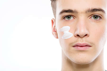 Close-up portrait of a young man with cosmetic cream on his face. Teenage guy cares about the cleanliness of the skin - isolated.の写真素材
