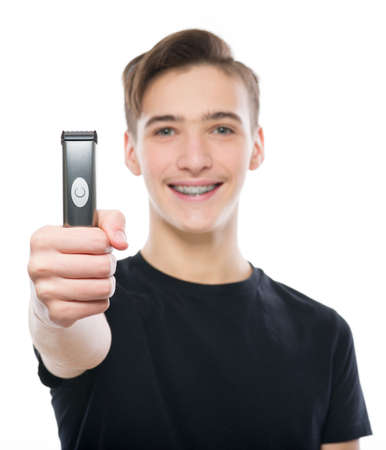 Smiling Teenage boy holds an electric razor in his hands, looking at camera - isolated on a white...