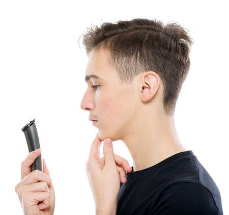 Teenage boy holds a razor and electric shaver in his hands, looking at camera - isolated on a white...