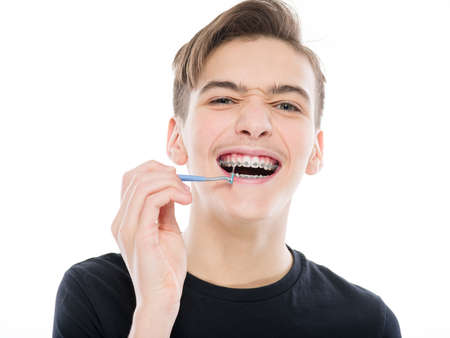Photo of a guy  cleaning braces.  Young man taking care of his teeth. Dental hygiene. Teenager brushes braces, isolated on white.の写真素材