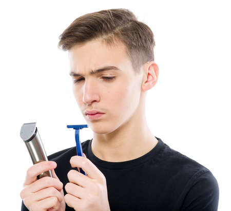 Teenager holds a razor and an electric razor while looking at the camera - isolated on a white...
