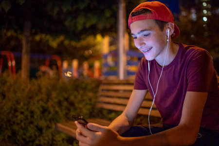 Portrait of a smiling young man with a smartphone, in the street.  Happy teenage boy is using mobile phone, outdoors. Cheerful teenager spends time in social networks using cell phone.の写真素材