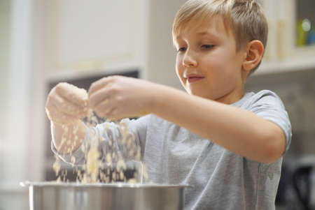 Child cooking at the kitchen. White boy stirring dough for a cookie. Kid is mixing ingredients for a cake in the steel bowl. 8 years old child cooking food at home.の写真素材