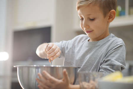 Child cooking at the kitchen. White boy stirring dough for a cookie. Kid is mixing ingredients for a...