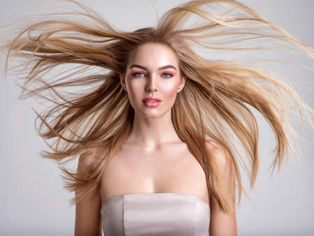 Portrait of a blonde beautiful woman with a long straight light hair. Woman with hair flying in the wind.  Portrait of a beautiful woman with a coral color makeup. Fashion model. Flying hair.の写真素材
