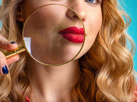 Woman checks skin face using loupe. Blonde holds a magnifying glass in front cheek. Young woman holds a magnifying glass in front of face. Beauty treatments. Adult girl zoom a part of skin face.の写真素材