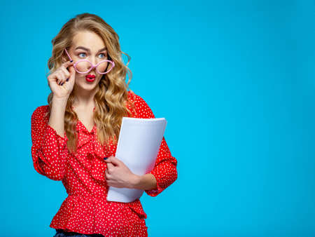 Surprised businesswoman in a casual clothes holds papers, at studio. Shocked woman secretary in a...