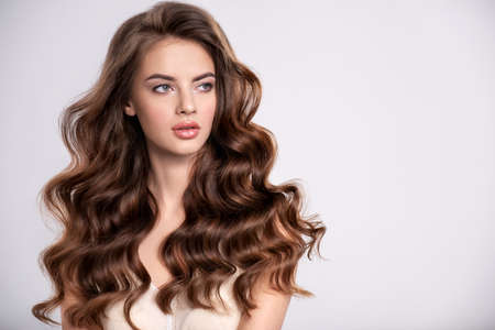 Portrait of a young beautiful woman with a long hair. Attractive fashion model with  brown hair - isolated on white background. Young girl with wavy hair looks to the camera.の写真素材