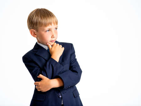 Confident blond boy dressed in a formal suit with blue tie lookinw away. Serious  kid in a blue business suit, posing at studio.  Photo of a cute little businessman boy.  Leader conception.の写真素材