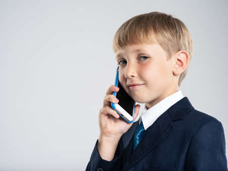 Photo of a  businessman  boy with smartphone .  Portrait of white  kid in a blue business suit holds...