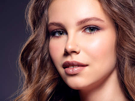 Beautiful brown-hair girl with long hair. Young fashion model posing in studio. Happy attractive woman with makeup looking at the camera. Close up face of a pretty caucasian girl smiling at camera.の写真素材