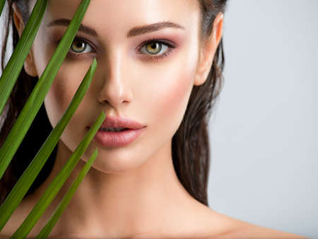 Young beautiful woman with healthy skin of face and palm leaves. Closeup fresh face of an attractive...