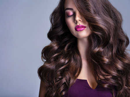Fashion model with wavy hairstyle. Attractive young  girl with curly hair posing at studio.  Face of a beautiful woman with long brown curly hair. Female face with purple makeup. Violet make-up.の写真素材
