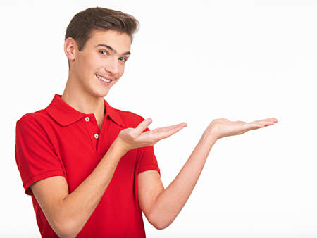 Portrait of happy young man holding something on palm, isolated over white background. Photo of smiling  handsome  guy in a red shirt presenting somethingの写真素材