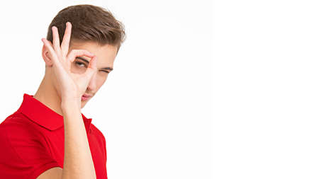 Portrait of happy young man showing okay gesture, isolated over white background. Photo of  Handsome white guy in a red shirt with sign OK.  Male person shows gesture OKAY .の写真素材