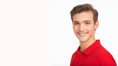 Photo of  young  happy man looking at camera. Side Portrait of smiling handsome guy posing at studio. Attractive male face with a smile. Teenager in a red shirt. Human face with a healthy teeth.の写真素材