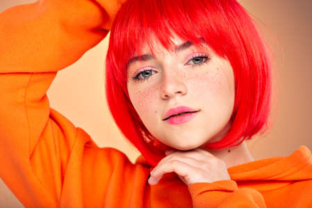 Closeup portrait of an young  girl with a red hair over colored background. Pretty teen girl with  freckles on face. Beauty portrait.  Photo of a young fashion model in orange clothes.の写真素材