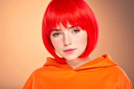 Closeup portrait of an young  girl with a red hair over colored background. Pretty teen girl with  freckles on face. Beauty portrait.  Photo of a young fashion model in orange clothes.の写真素材