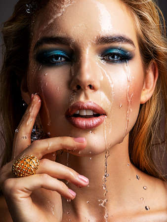 Photo of young woman with style make-up and water splashes  . Portrait of blonde woman with drops of water around her face. Sexy girl with blue eye makeup. Fashion model and water. Fashion concept.の写真素材