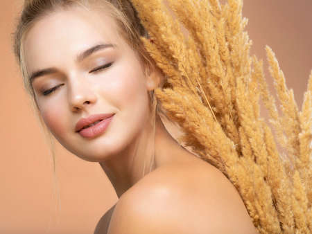 Calm Blonde girl with a bunch spring dry field flowers near the face - over colored background. Beauty face care concept. Young beautiful serene woman with a healthy  skin of the face, closed eyes.の写真素材