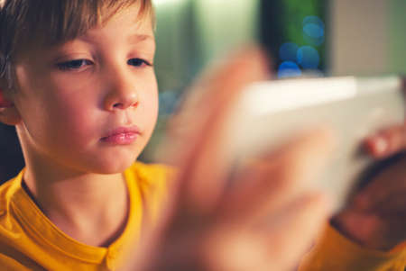 Close up face of a boy with smartphone playing a game, at home. Caucasian child spending time in a...
