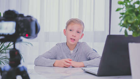 Child blogger videotapes his vlog at home. Boy recording his video blog. White boy speaks in front...