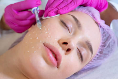 Cosmetologist applying a woman a cosmetic medical gel in a face from a syringe. Woman in a spa salon...