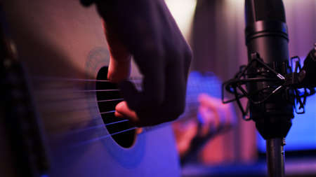 Close-up of the hands of a musician playing an acoustic guitar. Guitarist records music in the studio. Guitar and recording microphone close-up.の写真素材