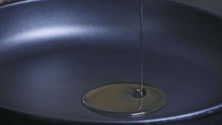 Pan with oil. Cook pours sunflower oil into a frying pan, macro shot.  Olive oil is poured into a...