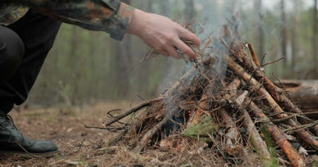Low angle shot of a man is trying make a fire in the forest. Close-up of a man's hand lighting a...
