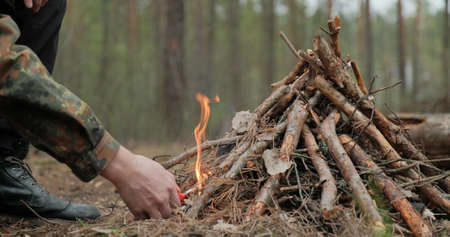 Man starts a fire in the forest using a lighter. Close-up of a man's hand lighting a fire with a lighter. Lighting a fire in the forest by a person. Low angle of a burning fire made of brushwood.の写真素材