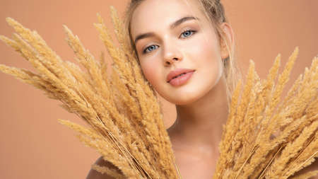 Closeup portrait of young beautiful woman with a healthy  skin of the face. Blonde girl with a bunch spring dry field flowers near the face - over colored background. Beauty face care concept.の写真素材