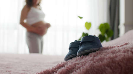 Children's shoes on the background of a pregnant woman expecting a child. Maternity prenatal care and woman pregnancy concept.の写真素材