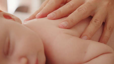 Mother doing massage on her healthy sleeping infant baby. Small caucasian newborn resting and laying on his belly while his mother is performing a massage for his small back and developing muscles.の写真素材