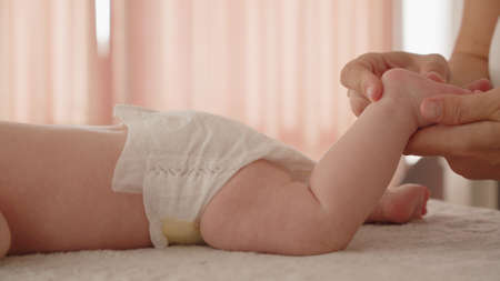 Mother doing massage for her healthy infant baby. Small caucasian newborn laying on his belly while his mother is performing a massage for his small feet and developing toes.の写真素材