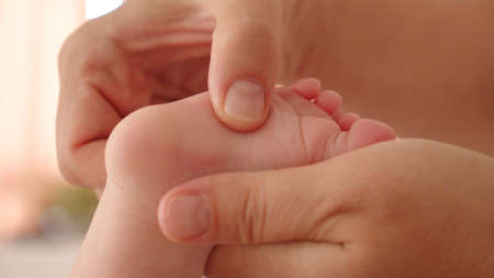 Mother doing massage for her healthy infant baby. Small caucasian newborn laying on his belly while his mother is performing a massage for his small feet and developing toes.の写真素材