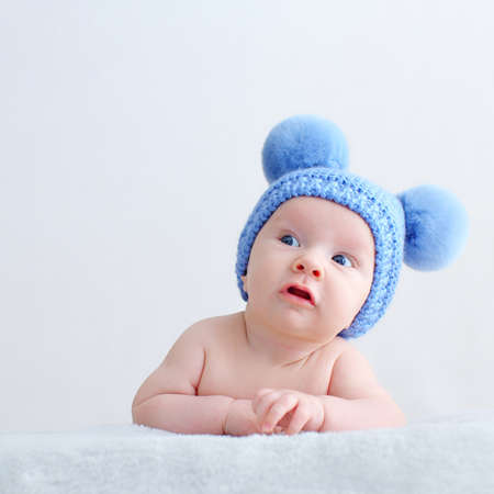 Sweet newborn baby in a blue hat with pompoms looks into the camera. Fun Beautiful, cute little infant with blue eyes looks into the camera.   A calm two-month-old kid is lying on a blanket.の写真素材