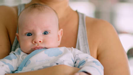 Newborn baby in her mother's arms. Mom holds the baby in her arms. The child looks into the camera. Infant with blue eyes happy being with mama. Maternity and childcare concept. Happy family moments.の写真素材
